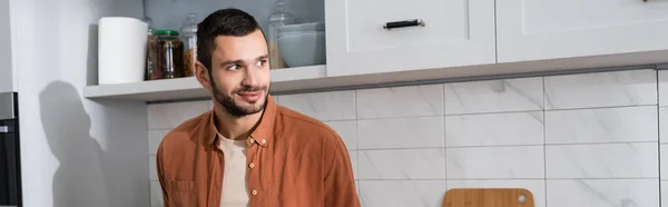 Uomo sorridente che guarda altrove in cucina, banner — Foto stock