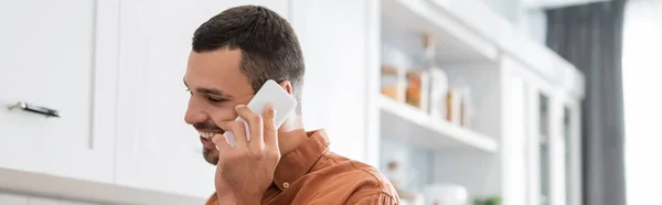 Веселый мужчина разговаривает по мобильному телефону на кухне, баннер — стоковое фото