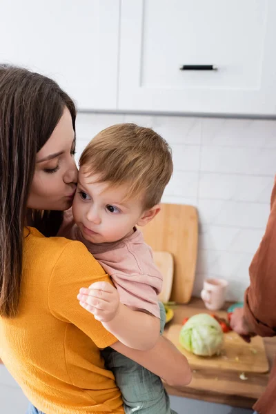 Woman kissing toddler son near husband in kitchen — Stock Photo