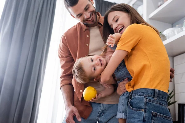 Happy child holding lemon near parents at home — Stock Photo