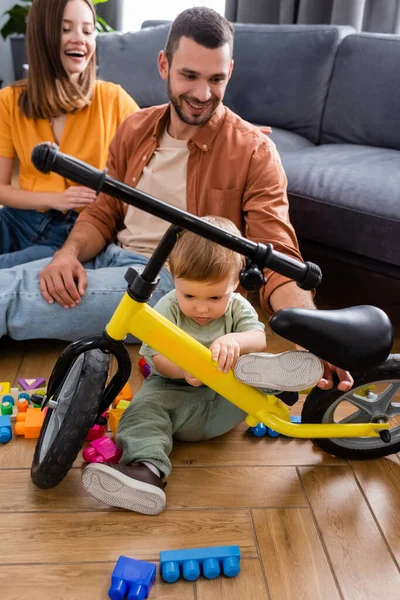 Kid looking at bike near parents and building blocks at home — Stock Photo