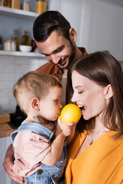 Woman biting lemon near toddler son and husband at home — Stock Photo