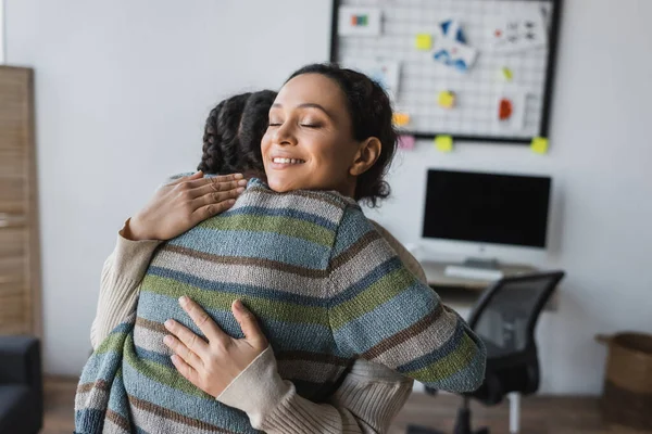 Happy african american mother with closed eyes hugging teen daughter at home — Stock Photo