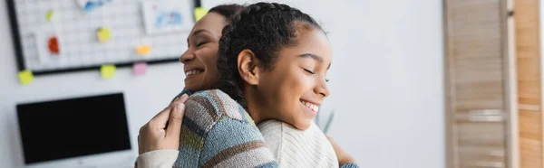 Mulher americana africana alegre e adolescente abraçando com os olhos fechados em casa, banner — Fotografia de Stock