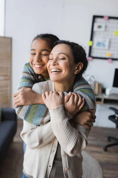 Menina americana africana feliz com os olhos fechados abraçando a mãe rindo em casa — Fotografia de Stock