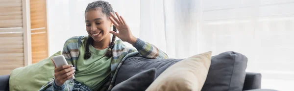 Feliz afroamericano adolescente agitando la mano durante la videollamada en el teléfono celular, pancarta - foto de stock