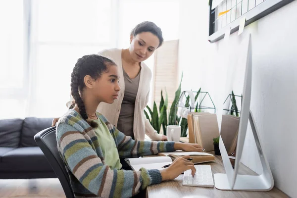 African american woman looking at teenage daughter doing homework on computer — Stock Photo