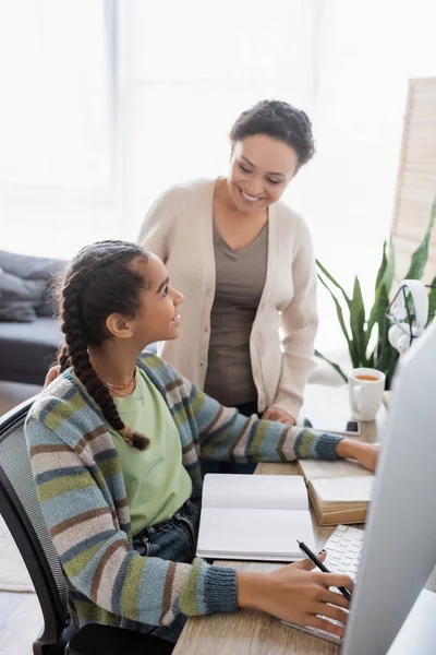 African american woman smiling near teenage daughter studying at home — Stock Photo