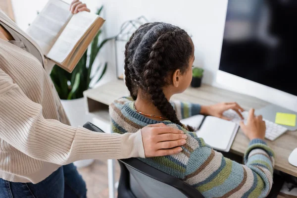 Menina americana africana fazendo lição de casa no computador perto da mãe com livro — Fotografia de Stock