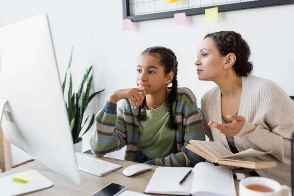 African american woman pointing with hand while helping teenage daughter doing homework — Stock Photo