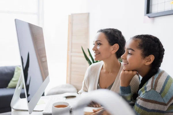 Cheerful african american mother and daughter looking at computer monitor while doing homework together — Stock Photo