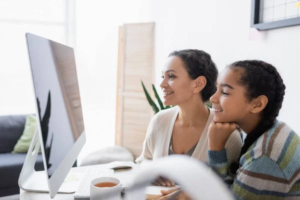 Alegre afro-americano mãe e filha olhando para monitor de computador enquanto fazendo lição de casa juntos — Fotografia de Stock