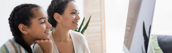 Smiling african american woman with teenage daughter looking at monitor with blank screen, banner — Stock Photo