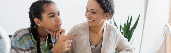 Afrikanerin zeigt auf verschwommenen Computermonitor neben lächelnder Mutter, Banner — Stockfoto