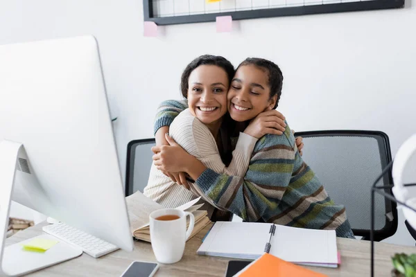 Happy african american mother and daughter embracing near computer and notebooks — Stock Photo