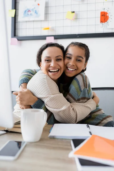 Glücklich afrikanisch-amerikanische Mutter und Tochter umarmen sich in der Nähe verschwommenen Computer zu Hause — Stockfoto