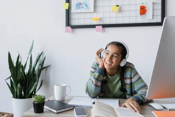 Smiling african american girl listening audio lesson in headphones while studying at home — Stock Photo