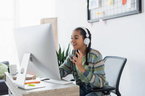 Aufgeregtes afrikanisch-amerikanisches Teenager-Mädchen mit Kopfhörern gestikuliert beim Blick auf den Monitor — Stockfoto