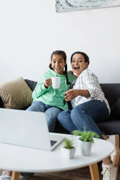 Animado afro-americano mulher rindo e apontando para laptop enquanto assiste filme perto adolescente filha — Fotografia de Stock