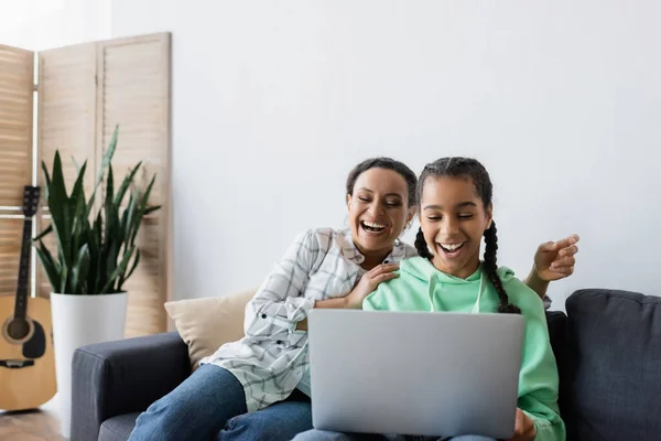 Joyeuse mère afro-américaine et sa fille regardant un film sur ordinateur portable à la maison — Photo de stock