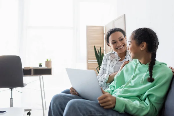 Cheerful african american mom and daughter looking at each other while watching movie on laptop — Stock Photo