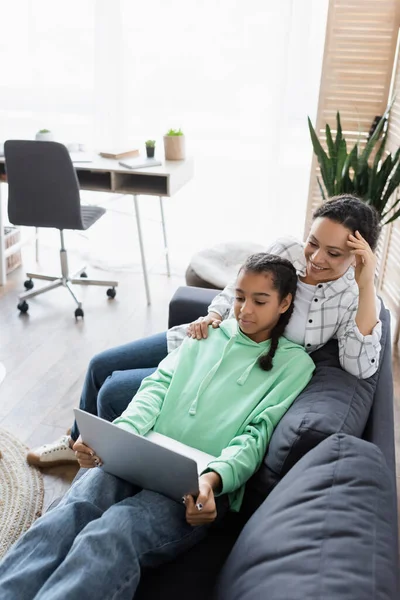 Vista ad alto angolo della ragazza afro-americana con madre che guarda film sul computer portatile sul divano — Foto stock