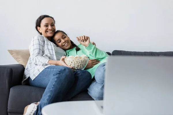 Feliz afro-americana mãe e filha com tigela de pipoca assistindo filme no laptop borrado — Fotografia de Stock