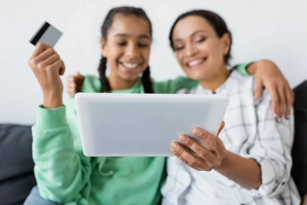 Verschwommene Afroamerikanerin hält digitales Tablet in der Nähe glücklicher Tochter mit Kreditkarte — Stockfoto