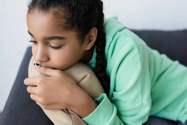Triste Africano americano adolescente menina abraçando travesseiro enquanto deitado em casa — Fotografia de Stock