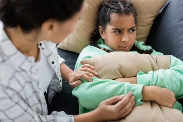 Verschwommene Afroamerikanerin beruhigt beleidigte Tochter, die mit Kissen auf Sofa liegt — Stockfoto