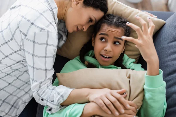 Afro-américaine femme apaisant fille irritée geste tout couché sur le canapé avec des oreillers — Photo de stock