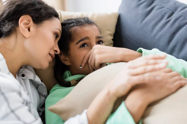 Africana americana mujer calmando molesto hija acostado en sofá y obscurecer la cara con la mano - foto de stock