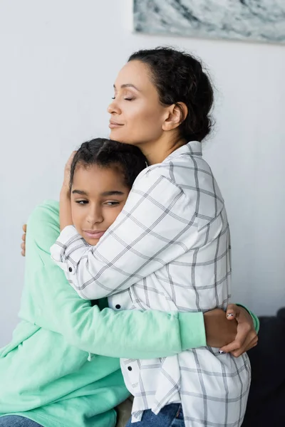 African american woman with closed eyes embracing frustrated daughter at home — Stock Photo