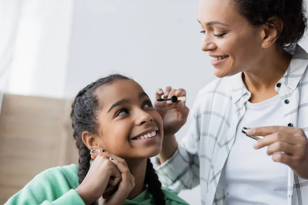 African american woman applying mascara on eyelashes of teenage daughter — Stock Photo