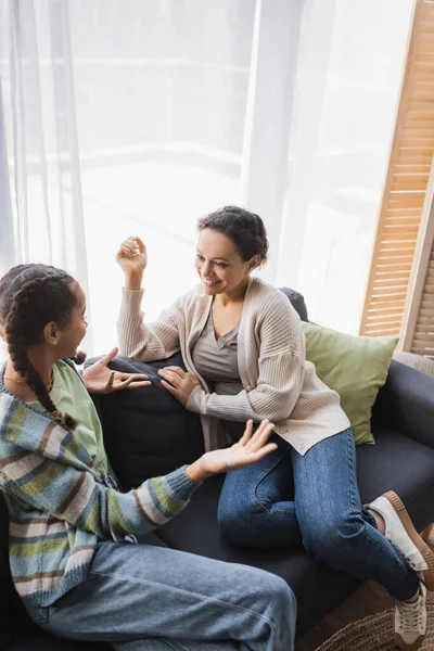 Vue grand angle de fille afro-américaine gestuelle pendant la conversation avec maman souriante à la maison — Photo de stock