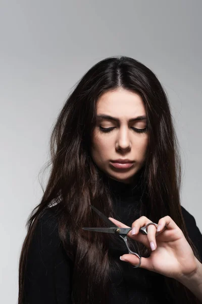 Young woman in black turtleneck holding scissors near long hair isolated on grey — Stock Photo