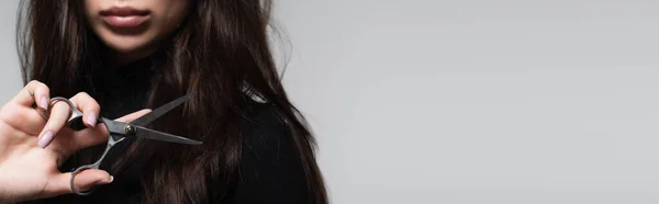 Vista ritagliata di giovane donna in dolcevita nero che tiene le forbici vicino ai capelli lunghi isolati su grigio, banner — Foto stock
