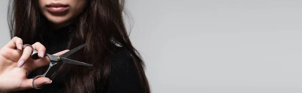 Cropped view of young woman in black turtleneck holding scissors near long hair isolated on grey, banner — Stock Photo