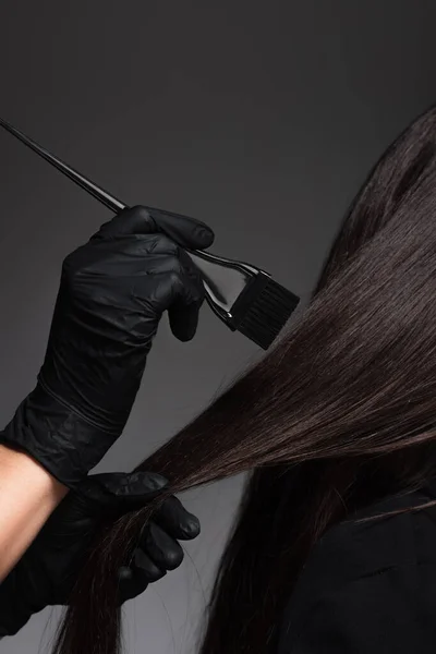 Vista parziale del pennello colorista vicino alla donna con i capelli castani isolati sul grigio scuro — Foto stock