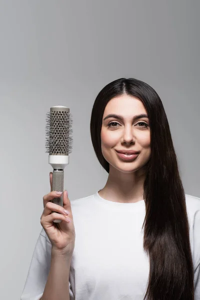 Pleased woman with smooth long hair holding thermal brush isolated on grey — Stock Photo