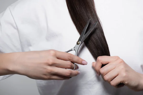 Cropped view of woman in white t-shirt holding scissors near shiny hair isolated on grey — Stock Photo