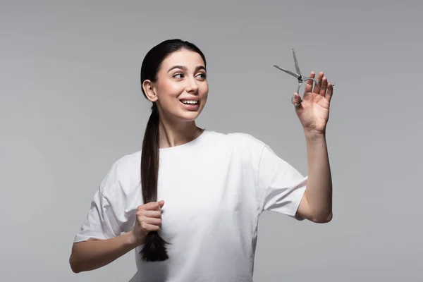 Fröhliche Frau mit glänzendem Haar, Schere isoliert auf grau — Stockfoto