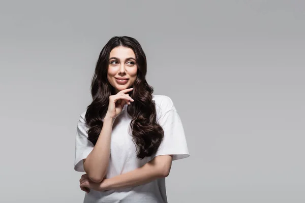 Giovane donna allegra con lunghi capelli ondulati distogliendo lo sguardo isolato sul grigio — Foto stock