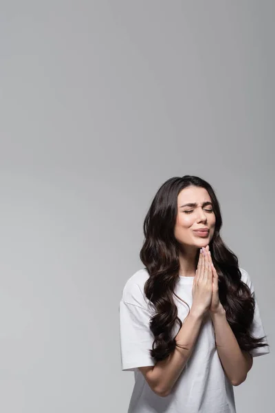 Young woman with long wavy hair standing with praying hands isolated on grey — Stock Photo