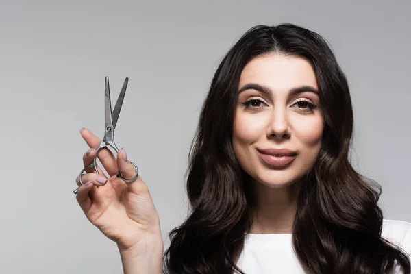 Smiling woman with wavy hair holding scissors isolated on grey — Stock Photo