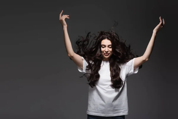 Jeune femme souriante aux cheveux ondulés gesticulant sur gris foncé — Photo de stock