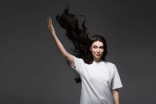 Jeune femme souriante aux cheveux ondulés et la main levée sur gris foncé — Photo de stock