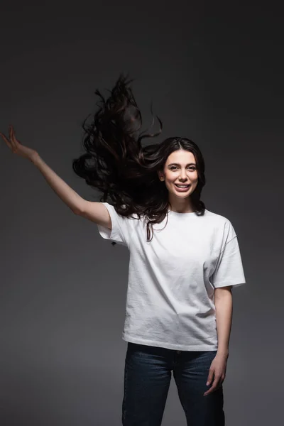 Giovane donna felice con i capelli ondulati e mano alzata su grigio scuro — Foto stock