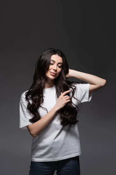 Joven mujer alegre con el pelo ondulado mirando hacia abajo en gris oscuro - foto de stock