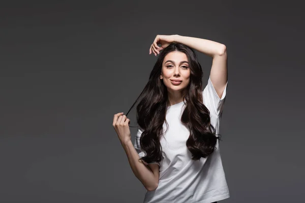 Giovane donna soddisfatta con i capelli ondulati guardando la fotocamera su grigio scuro — Foto stock